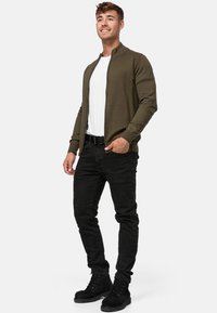 Maslinasto zelena zip-up cardigan preko bijele majice, uparen s crnim trapericama i crnim čizmama. Jednostavan dizajn s rebrastim manžetama i ovratnikom.