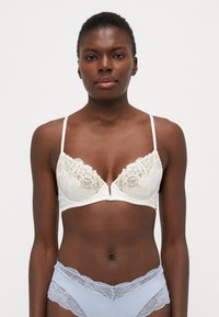 Soutien-gorge en dentelle blanche avec un décolleté en V profond et des bretelles fines. Présente des accents en dentelle florale et une finition en tissu lisse.