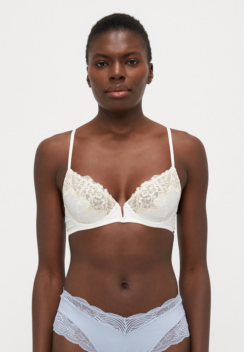 Soutien-gorge en dentelle blanche avec un décolleté en V profond et des bretelles fines. Présente des accents en dentelle florale et une finition en tissu lisse.