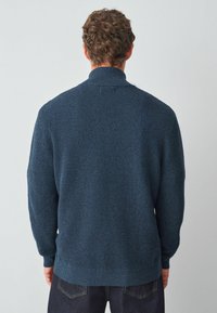 Granatowy sweter dzianinowy o teksturowanym wykończeniu, z prążkowanymi mankietami i dołem, z szerokim kołnierzem. Widok z tyłu.