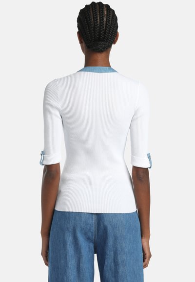 Haut blanc côtelé à manches courtes, avec un accent en denim sur les poignets et un col arrondi, mettant en valeur une silhouette ajustée.