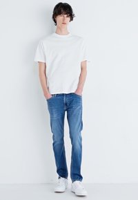 Bela bombažna majica, modri jeans z rahlim zbledelostjo in bele superge. Preprost dizajn, ravno prileganje, kratki rokavi.