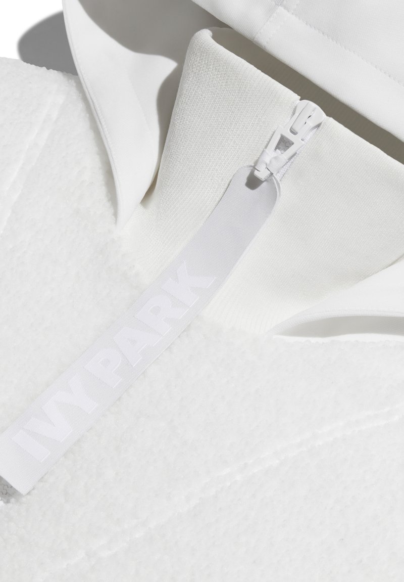 Biały sweatshirt z kapturem, z zamkiem błyskawicznym i teksturowanym materiałem. Metka przedstawia napis "IVY PARK" w wyraźnym, białym druku.