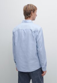 Light blue, long-sleeve shirt made of soft fabric. Features a button-down collar and cuffed sleeves, with a straight hem at the back.