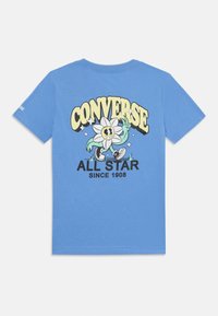 T-shirt en coton bleu clair avec un imprimé graphique d'un personnage de fleur en dessin animé et le texte "CONVERSE ALL STAR SINCE 1908" en dessous.