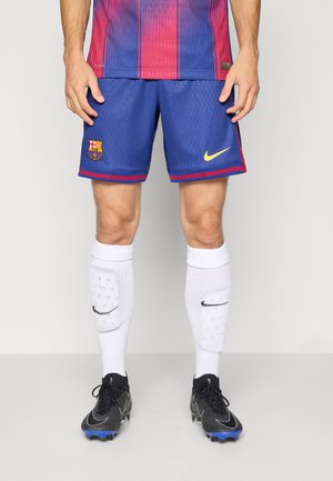 Pantaloni corti blu del FC Barcelona con dettagli rossi, logo Nike e stemma della squadra. Calze bianche, scarpe nere con dettagli blu. Tessuto a rete, vestibilità atletica.