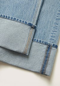 Tissu en denim bleu clair avec des coutures contrastantes orange et grises. Un revers est plié, montrant une finition nette et la texture.