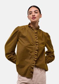Chemisier vert olive avec manches bouffantes, en tissu texturé, et patte de boutonnage froncée à l'avant. Présente des fermetures à boutons et un col haut.