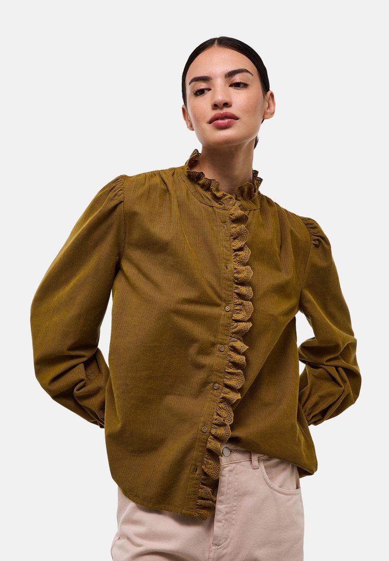Chemisier vert olive avec manches bouffantes, en tissu texturé, et patte de boutonnage froncée à l'avant. Présente des fermetures à boutons et un col haut.
