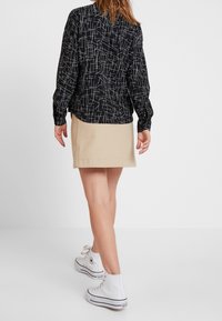 Giacca nera con motivi lineari bianchi, gonna beige e sneakers alte bianche. Il tessuto sembra strutturato, con maniche lunghe e design aderente.