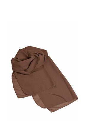 Femme aux cheveux blonds portant une robe longue marron fluide bustier, des sandales à talons hauts dorées, de grandes boucles d'oreilles en or et un bracelet en or.