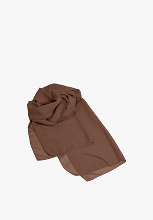 Femme aux cheveux blonds portant une robe longue marron fluide bustier, des sandales à talons hauts dorées, de grandes boucles d'oreilles en or et un bracelet en or.