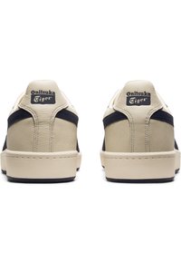 Onitsuka Tiger sneakers with a beige leather upper, navy accents, and rubber sole. Notable logo on the heel, classic low-top design.