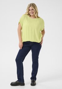 Limegrøn bluse med korte ærmer og afslappet pasform, kombineret med mørkeblå lige ben jeans og sorte platform sko. Enkel, struktureret design.