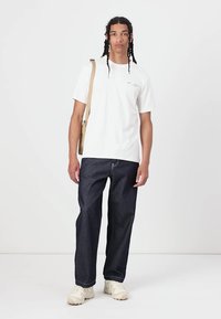 Hvid bomulds t-shirt med korte ærmer, mørkeblå denim bukser og beige sneakers. En beige crossbody taske hænger over skulderen.