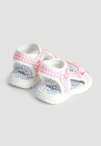 Biele sandále s rúžovými kockovanými popruhmi a vzorovanou insole. Majú nastaviteľné uzávery na suchý zips a polstrovanú podrážku.