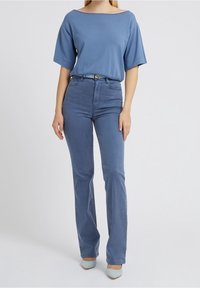 Modrá tričko s širokým výstřihem a volným střihem, kombinované s modrými flared džíny s vysokým pasem a světle modrými podpatky.