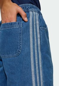 Shorts in denim blu con vestibilità rilassata, fascia elastica in vita, tasche laterali e tre strisce bianche verticali lungo la cucitura laterale.