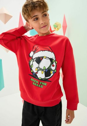 Roter Sweatshirt mit einem Grafik von einem Fußball, der in Weihnachtslichter und einen Weihnachtsmann-Hut eingewickelt ist. Der Text lautet "DECK THE BALLS." Glatte Textur, lange Ärmel.