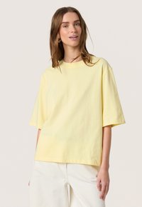 Tricou din bumbac galben, cu o croială lejeră, m�âneci scurte și decolteu rotund, asortat cu pantaloni de culoare deschisă, design minimalist.