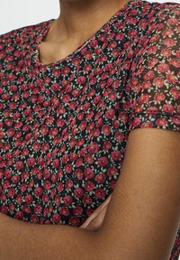 Haut fleuri avec un fond marine, orné de petites fleurs rouges et de feuilles vertes, à manches courtes et col rond. Tissu léger.