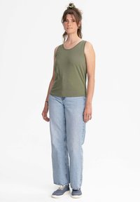 Olijfgroen mouwloos tanktop met een ronde hals, gecombineerd met lichtblauwe rechte jeans en grijze sneakers.