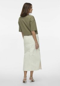 Top corto de manga corta a rayas olivo combinado con una falda de mezclilla blanca de longitud media con una abertura lateral. El modelo lleva sandalias de tacón beige.