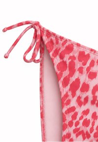 Bas de bikini à imprimé léopard rose et rouge, avec détail de lien noué sur le côté et coutures visibles sur fond blanc.