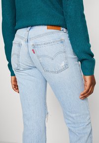 Světle modré džíny s rovný fit, s hnědou koženou nášivkou, dvěma zadními kapsami a jemným opotřebením podél boční švy.