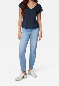 T-shirt blu navy con scollatura a V e maniche corte, abbinato a jeans a gamba dritta azzurri e sneakers bianche con dettagli neri.