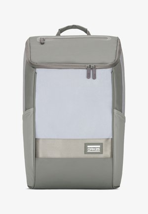 Zaino grigio con un esterno in tessuto liscio, dotato di un ampio scomparto principale, più zip e un patch con logo frontale.