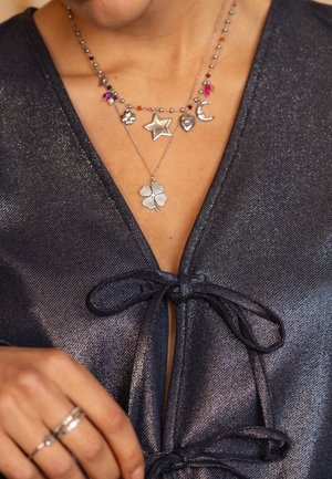 Collar de encanto de plata con estrella, corazón, luna creciente, flor y trébol de cuatro hojas sobre una cadena de cuentas, llevado sobre una blusa navy brillante.