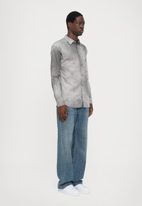 Grå skjorte med knapper og subtile mønstre, kombinert med løse lyseblå denimbukser og hvite sneakers.