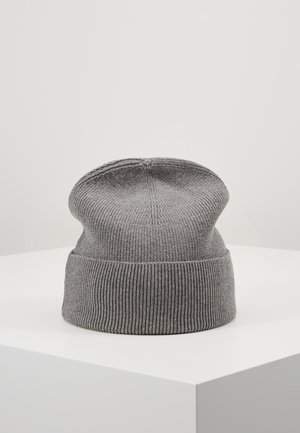Bonnet gris en maille côtelée avec revers, présenté sur un socle blanc devant un fond gris clair uni.