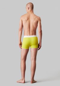 Boxer briefs gialli con una vita bianca, caratterizzati da una texture liscia e un design aderente, visti da dietro.