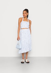 Top crop floral azul e saia midi combinando, feitos de um tecido leve, acompanhados de uma bolsa azul clara e sandálias brancas com solas pretas.