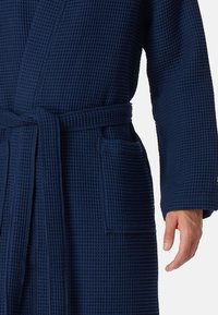 Accappatoio in tessuto a nido d'ape blu navy con cintura, tasca laterale e tessuto testurizzato. Presenta maniche lunghe e una vestibilità rilassata.
