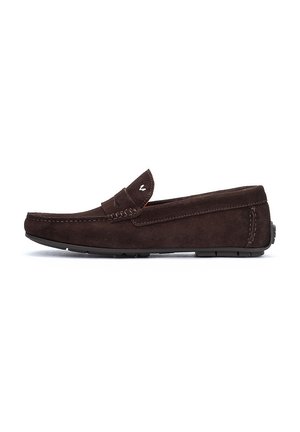 Mocasines de ante marrón con un diseño plano, detalles de costura y un pequeño emblema en la parte superior. La suela es de goma texturizada para un mejor agarre.