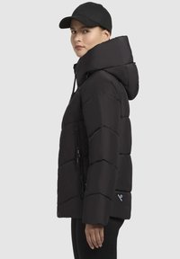 Zwarte donzen jas met een capuchon, voorzien van een ritssluiting, zigzag stikpatroon en een zijvak. Gemaakt met een zwarte pet.