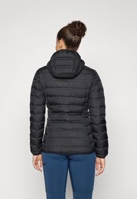 Veste noire rembourrée avec capuche, présentant des sections matelassées, une silhouette ajustée et une texture lisse. Coutures visibles et poche zippée.