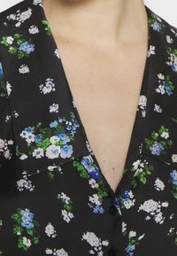 Gros plan d'un vêtement noir avec un imprimé floral bleu, blanc et vert et un col en V profond sur peau nue.