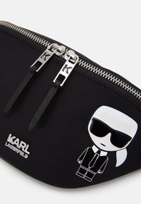 Zwarte nylon pouch met zilveren rits, met een cartoon avatar, het logo "KARL LAGERFELD" en textuur ritstrekken.