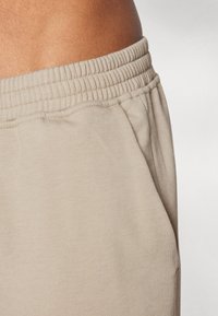 Beige Jogginghosen mit einer weichen, glatten Textur, elastischem Bund und Seitentaschen, ausgestattet mit einer figurbetonten Passform und minimaler Nahtführung.