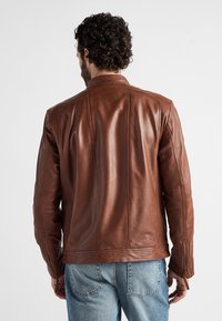 Braune Lederjacke mit strukturiertem Design, markanten Nähten und Reißverschlussärmeln. Die Rückseite zeigt eine glatte Textur.