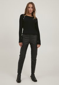 Schwarzer gerippter Pullover mit metallischen Akzenten an den Schultern, kombiniert mit schwarzen Lederhosen und Stiefeletten. Glatte Textur, taillierte Passform.
