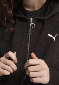Czarna hoodie na zamek błyskawiczny z teksturowanej tkaniny, srebrnym zamkiem i okrągłym uchwytem, z białym logo Puma na klatce piersiowej.