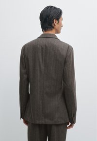Brauner Blazer mit Streifenmuster, ausgestattet mit einem Reverskragen, strukturierten Schultern und einer einzelnen Knopfverschlüssen, gefertigt aus einem texturierten Wollmischgewebe.