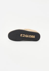 Tan skate shoe with a rubber black outsole, featuring a textured pattern and logo detail. The upper has perforations for breathability.