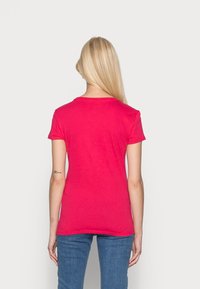 Camiseta de manga corta en magenta con cuello redondo, hecha de algodón suave, que cuenta con una espalda sin costuras y un diseño ajustado.