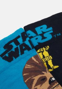 Dvojica ponožiek s farebnými vzormi. Jedny sú modré so vzorom Chewbaccu, druhé sú čierne so žltými detailmi Stormtroopera.